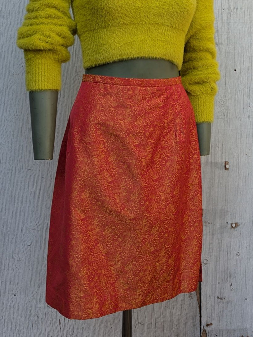 Mannequin wearing a yellow fuzzy sweater and red patterned skirt against a textured white wall.