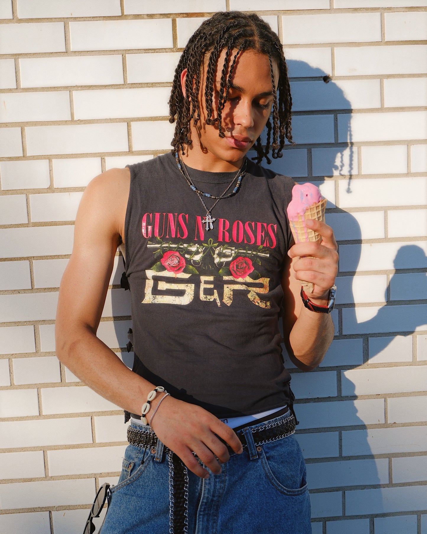 Man wearing a tank top with 'Guns N' Roses' graphic against a white brick wall