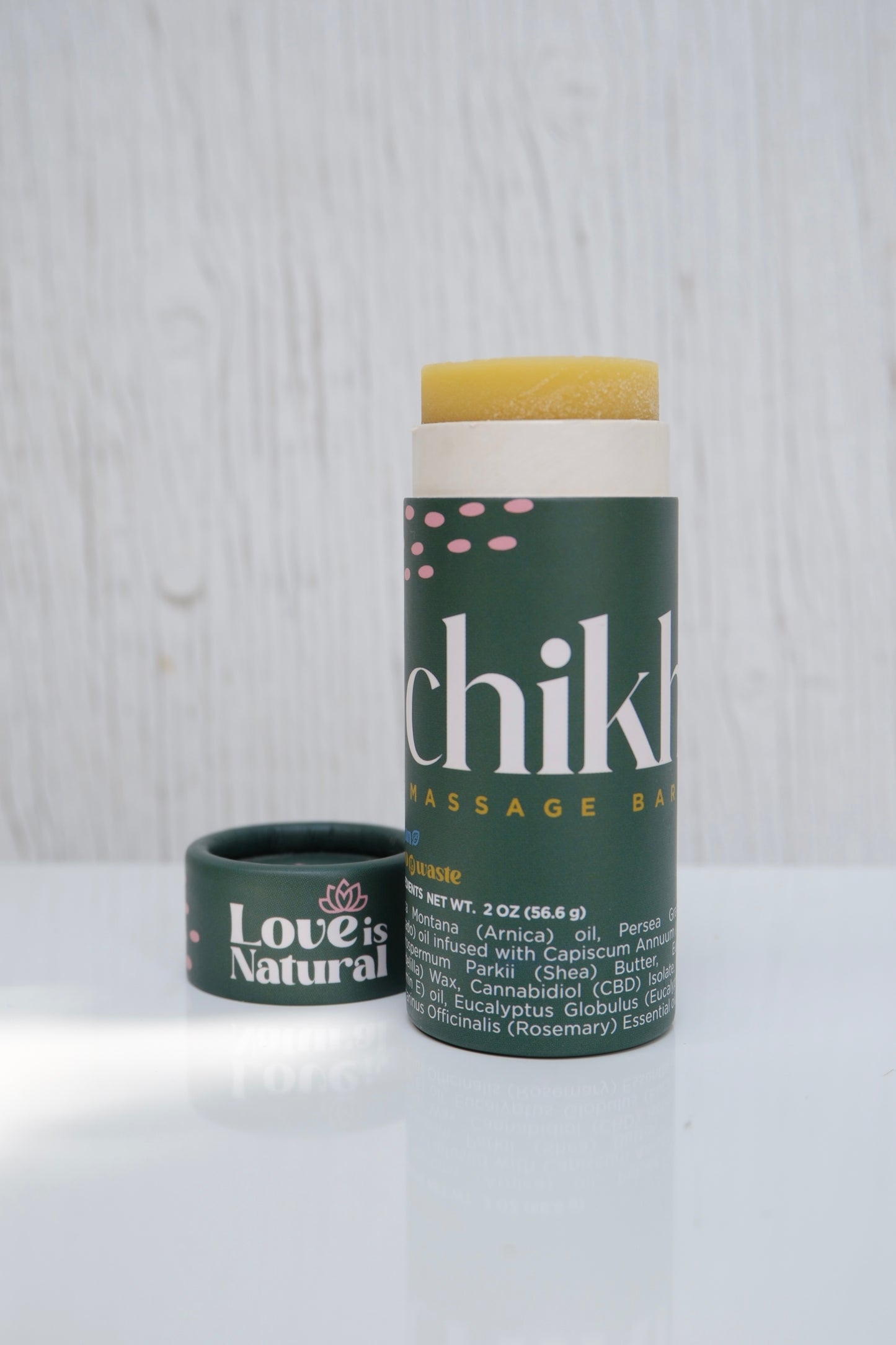 Green cylinder massage stick labeled with 'Chikhuya' branding and 'Love is Natural' on the cap on a light wooden surface.