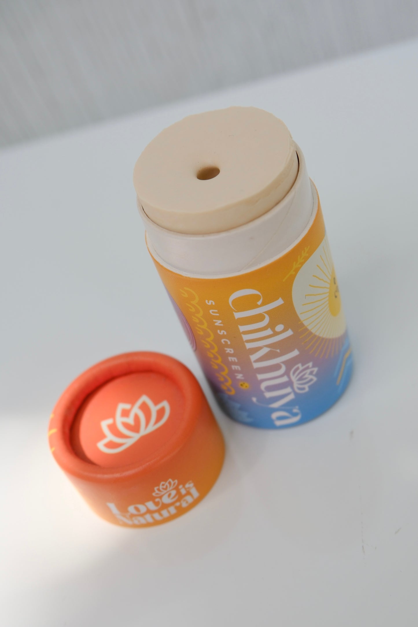 Cylinder stick of sunscreen with cap off and 'Chikhuya' colourful orange, yellow, and blue branding on a light gray background