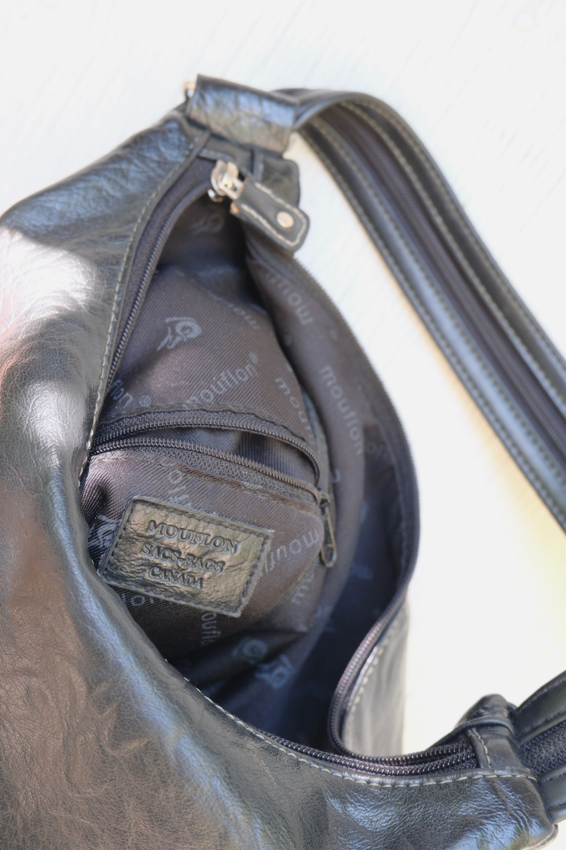 Black faux leather bag with a visible Mouflon brand logo on a white background