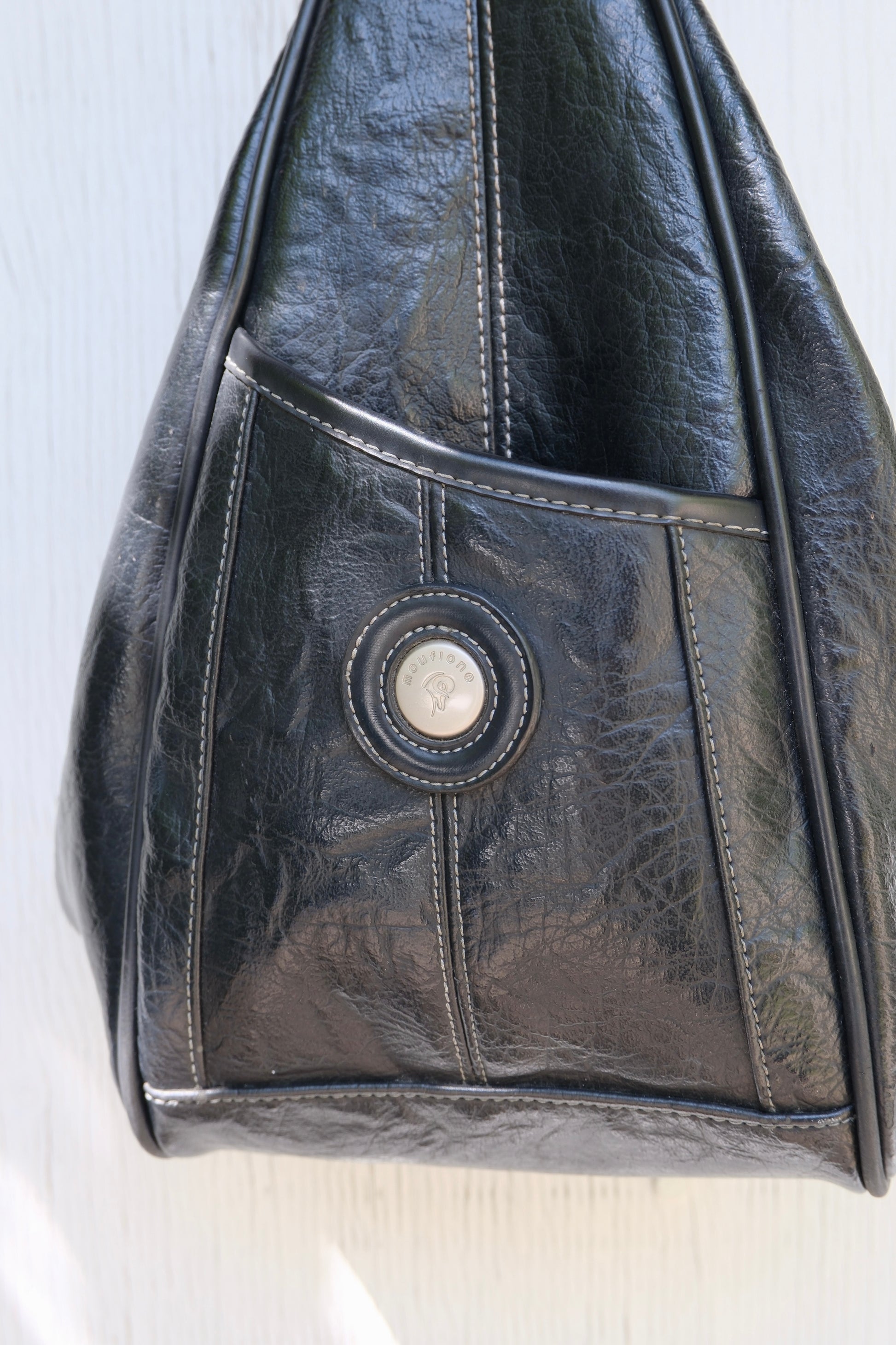Black faux leather bag with a circular metal logo on a white background