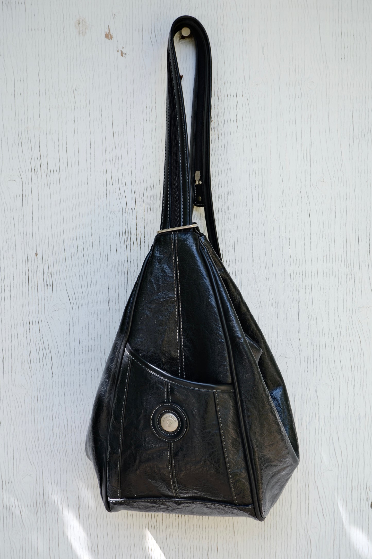 Black faux leather bag hanging on a light wooden background