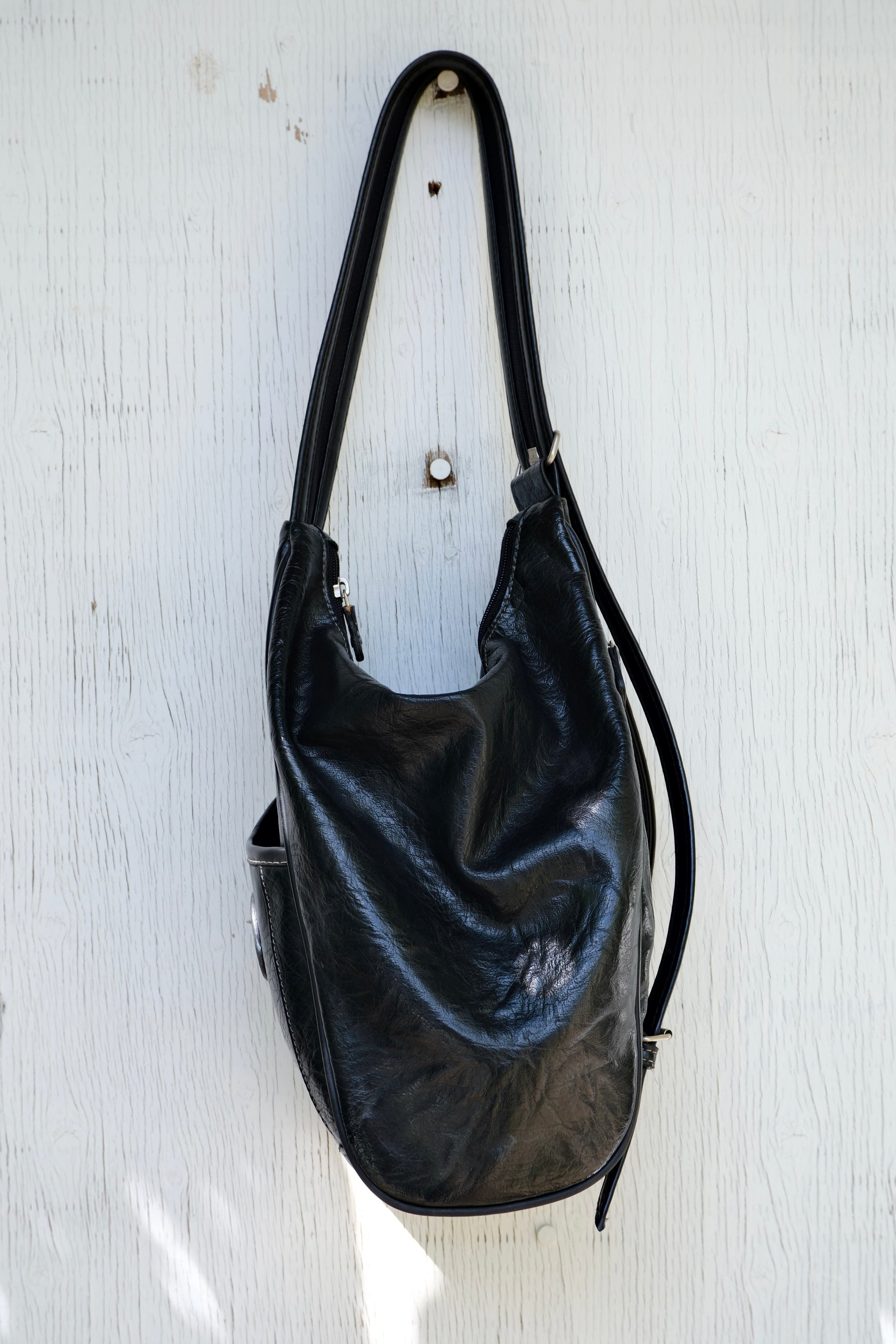 Side view of a black faux leather bag hanging on a light wooden background
