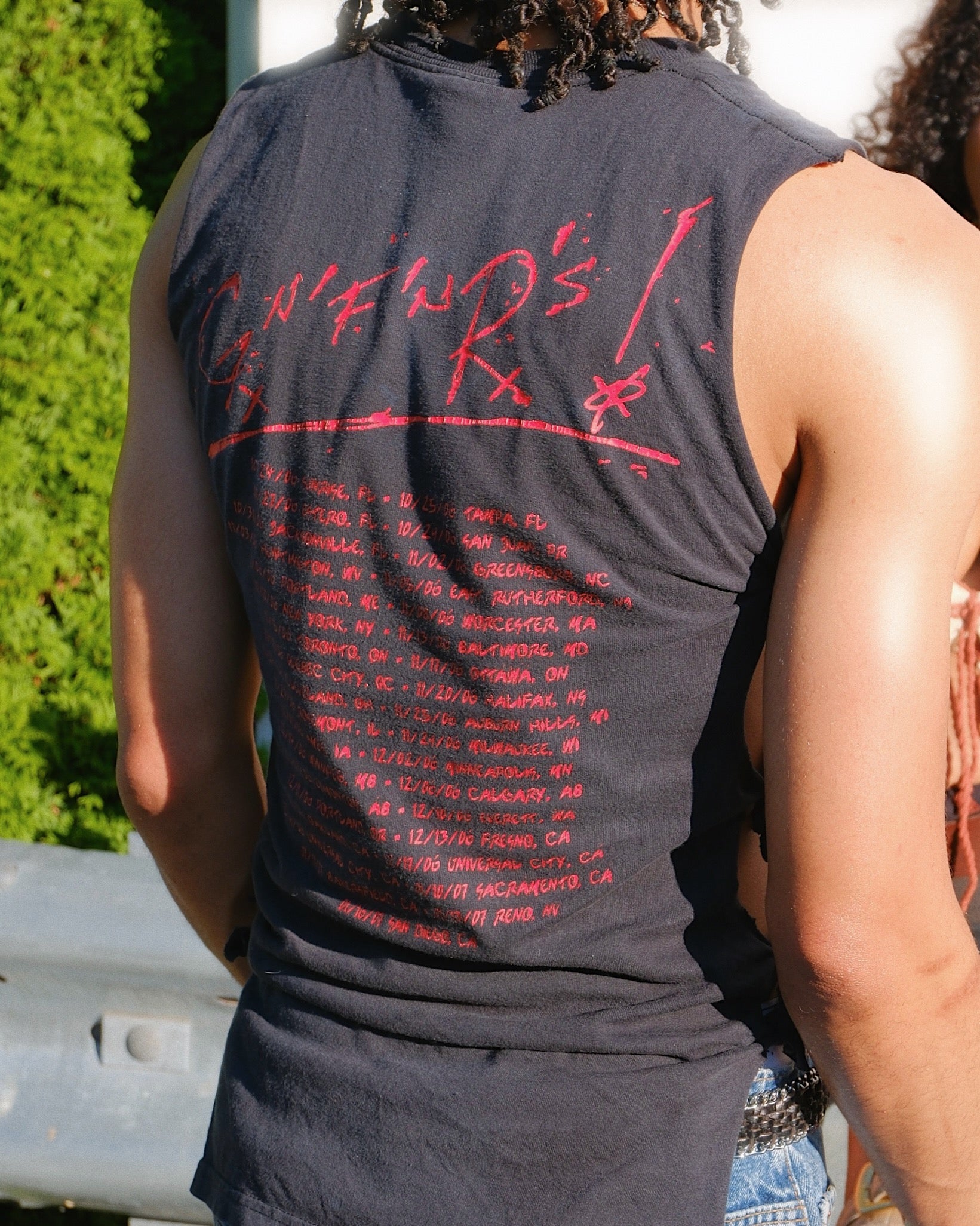 Man is standing outside wearing a 'Guns N' Roses' tank top with tour dates listed on the back in red text