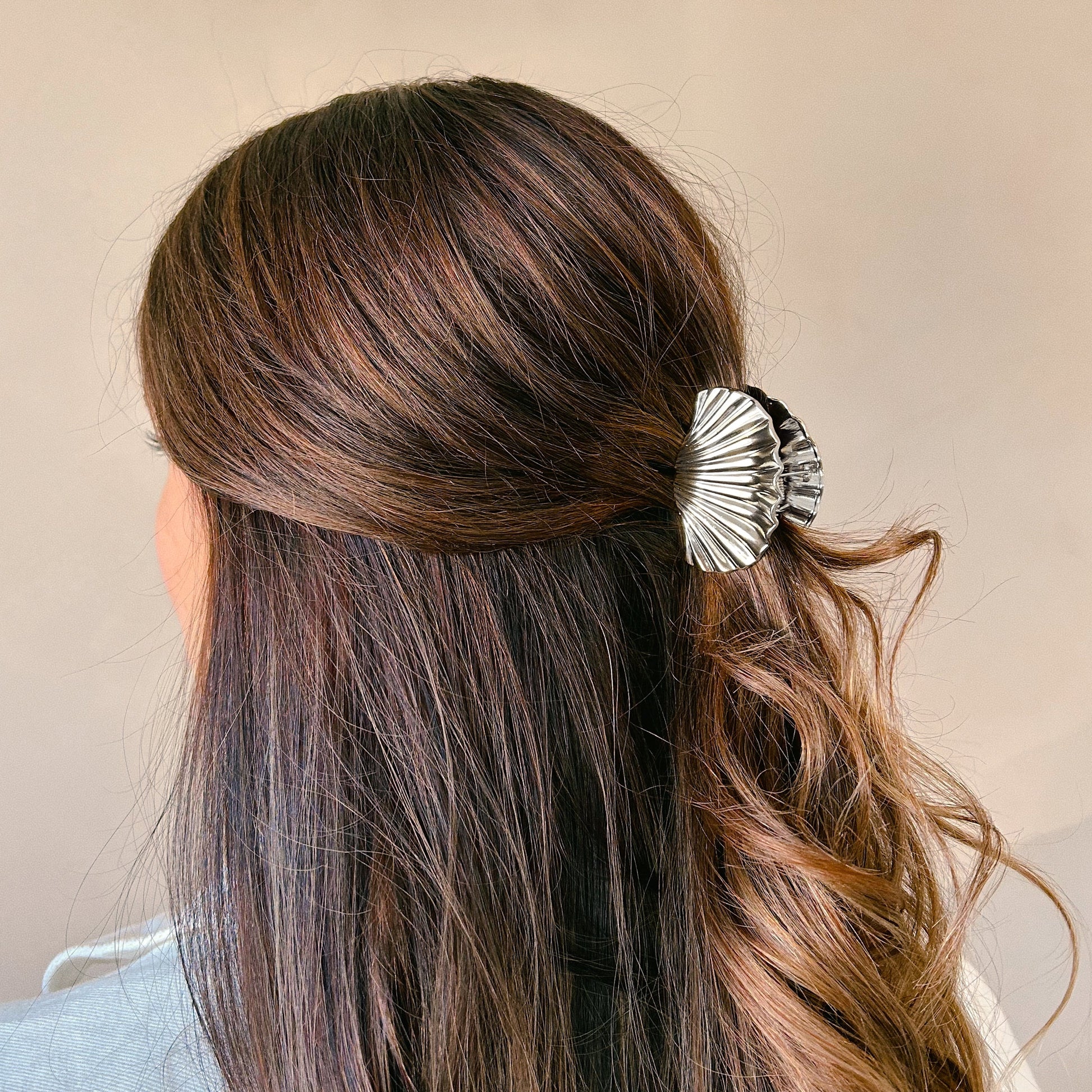 Woman with dark brown wavy hair wearing a silver shell-shaped hair clip against a neutral background